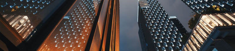 Low angle view of modern skyscraper buildings illuminated at night reflecting on a glass facade 